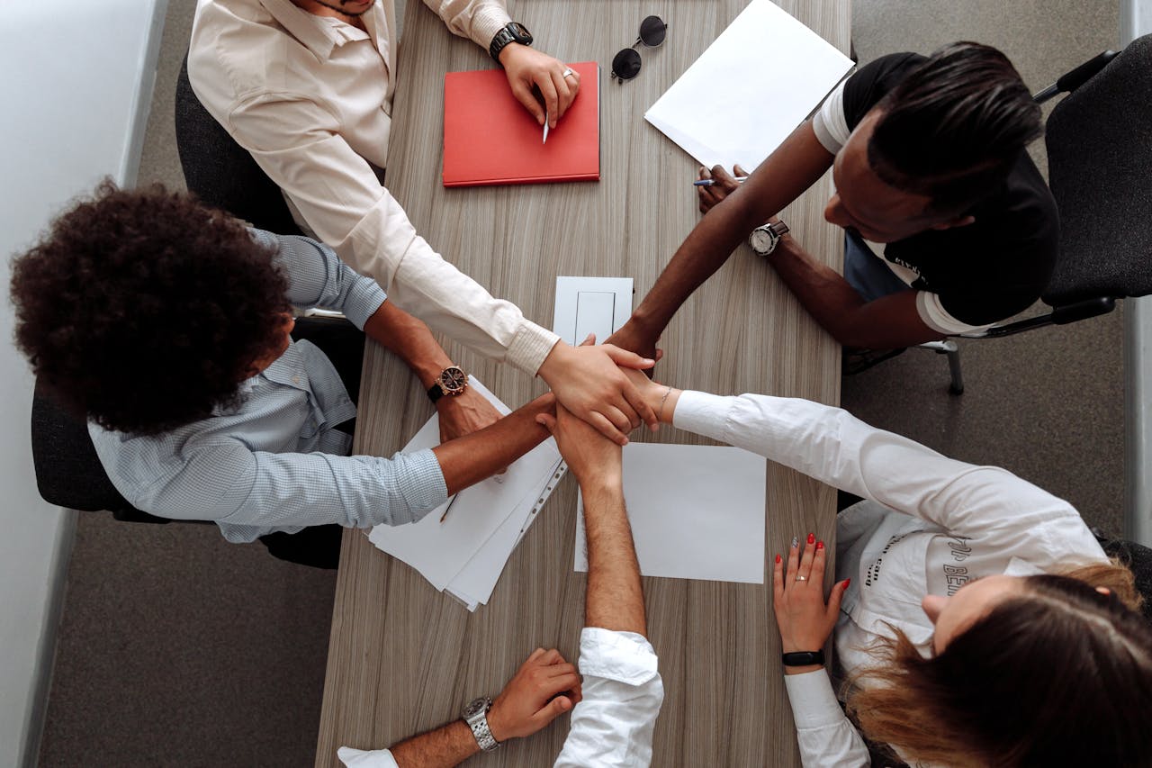 hero-img-02 Overhead view of a diverse team placing hands together in a sign of unity during a meeting.