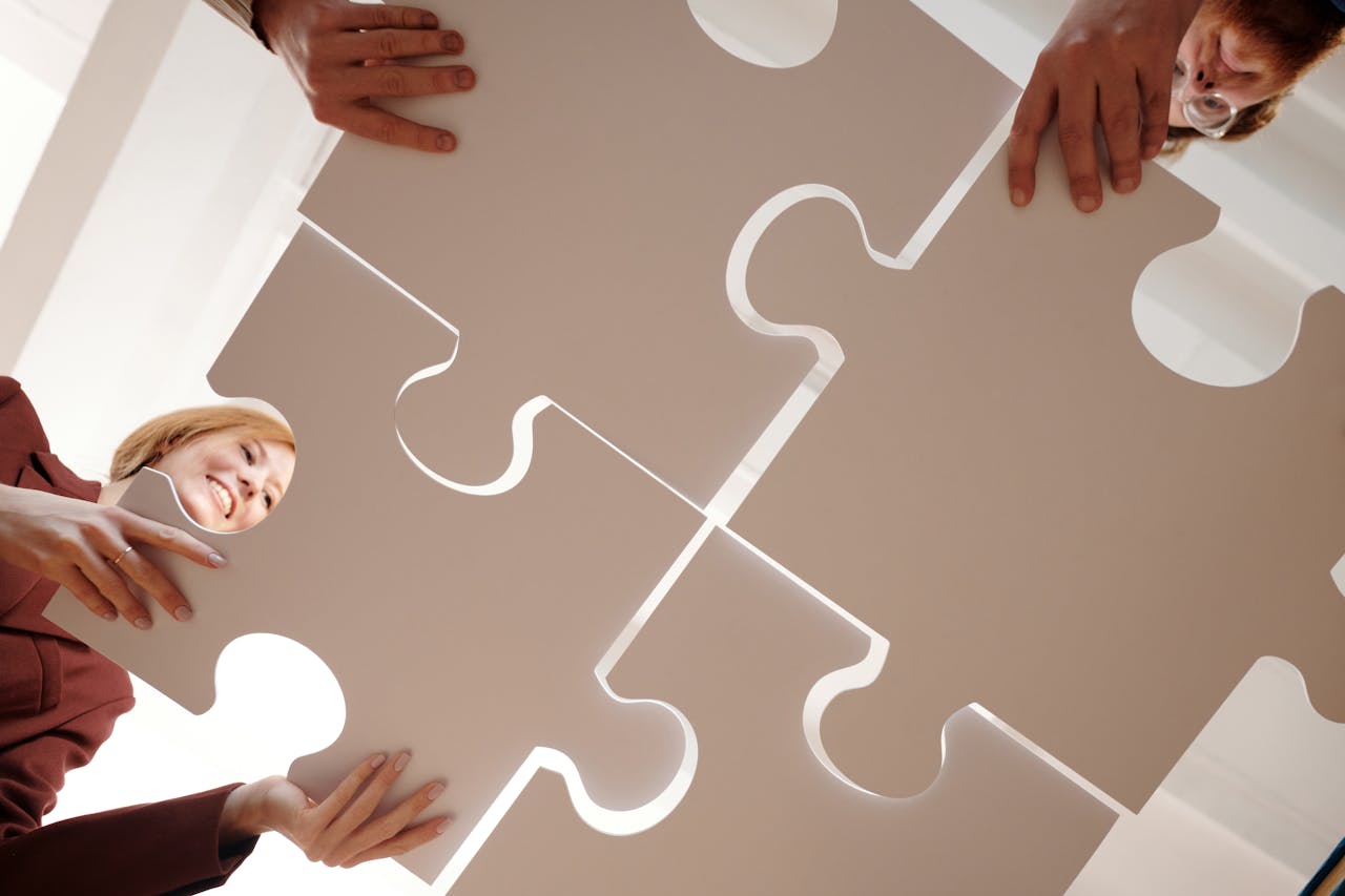 hero-img-01 Low angle view of diverse team assembling large puzzle pieces, symbolizing unity and cooperation.